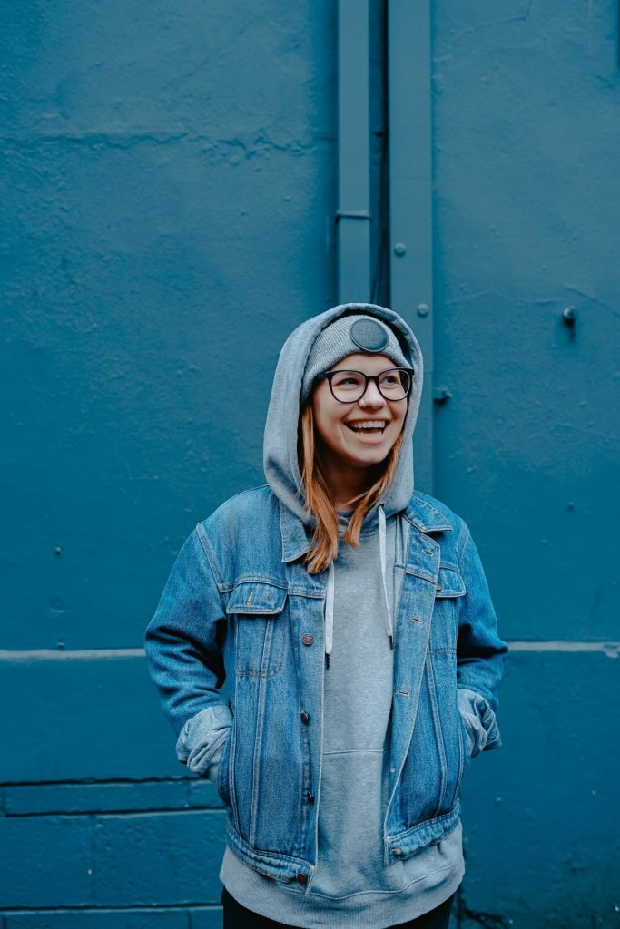 Adolescente sorrindo, de jaqueta jeans, em frente a uma parede azul