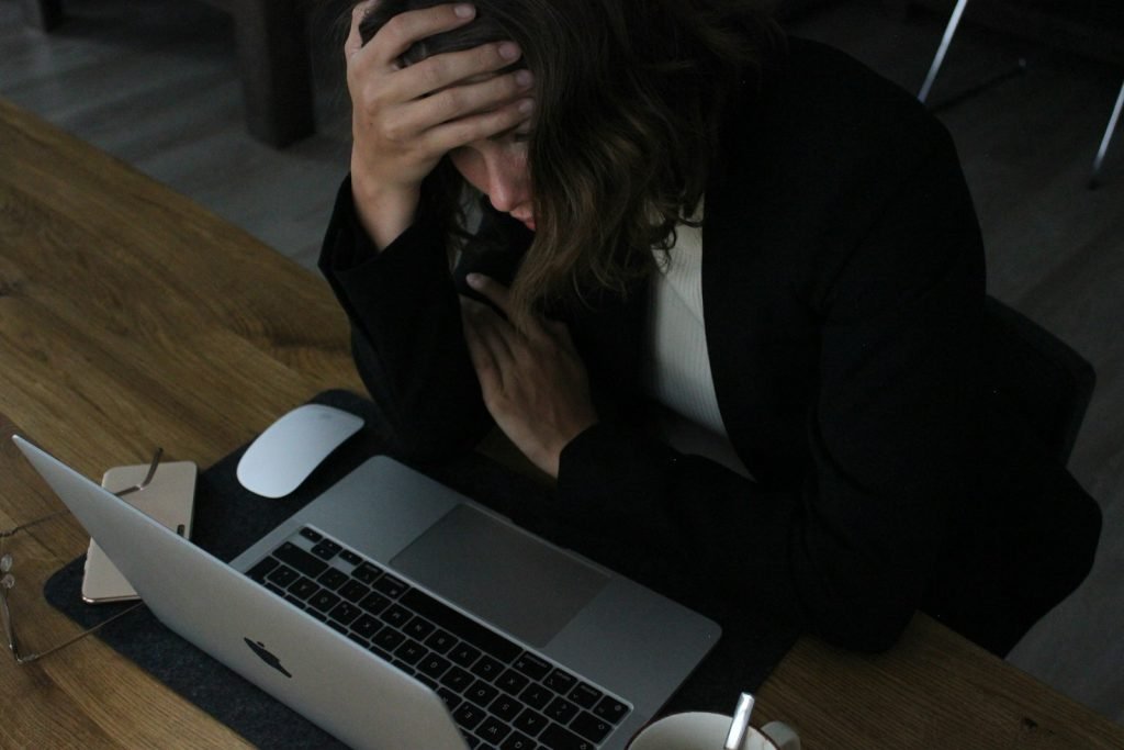 Pessoa com as mãos na cabeça diante do notebook, esgotada pelo trabalho